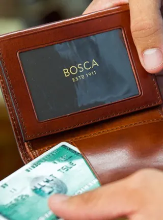 Close up shot of hands holding a brown leather wallet with Bosca inscribed on the inside