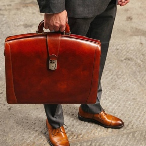 Lower half of man wearing a suit holding a dark brown leather briefcase