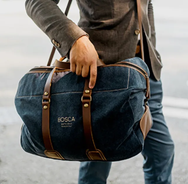 Man walking and reaching into dark blue and brown leather duffle bag